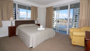 Una habitación de hotel con una cama grande, un sillón amarillo y un balcón con vistas a la ciudad.