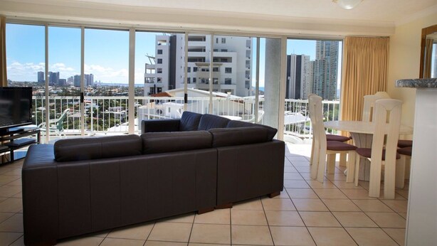 Una sala de estar moderna con un sofá grande, una mesa de comedor con sillas y un balcón con vistas al horizonte de la ciudad.