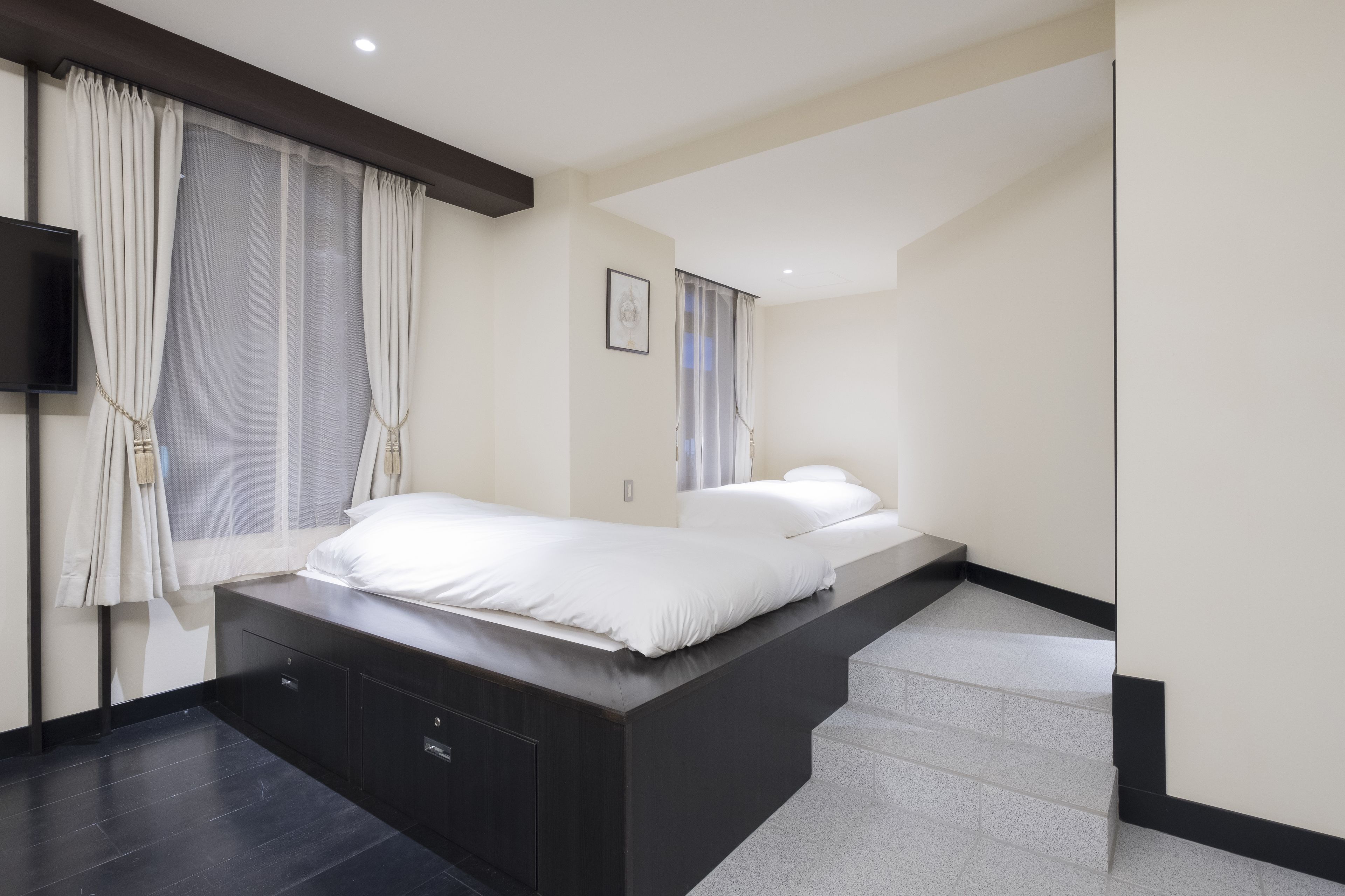 A modern bedroom with a bed, built-in storage, a flat-screen TV, and a staircase leading to an upper level.