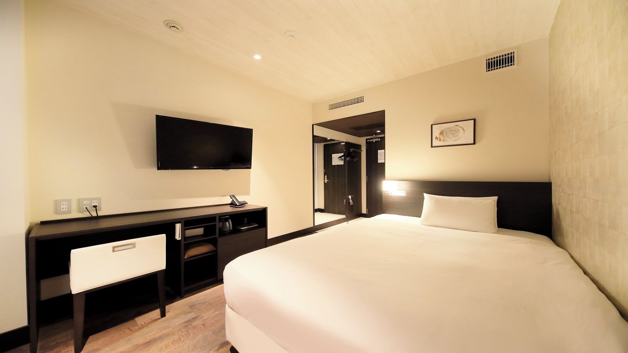 Habitació d'hotel amb llit, escriptori, cadira, televisió i mirall.