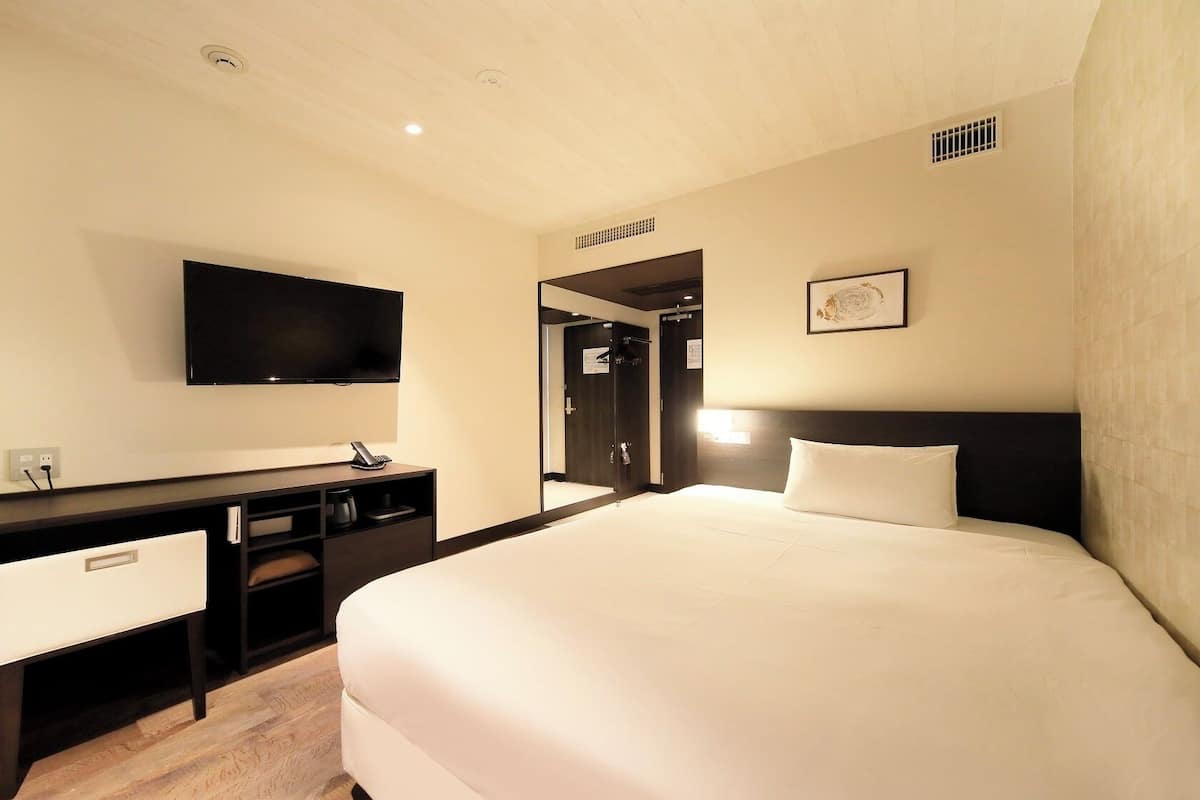 Ein Hotelzimmer mit einem Bett, einem Schreibtisch, einem Sessel, einem Fernseher und einem Spiegel.