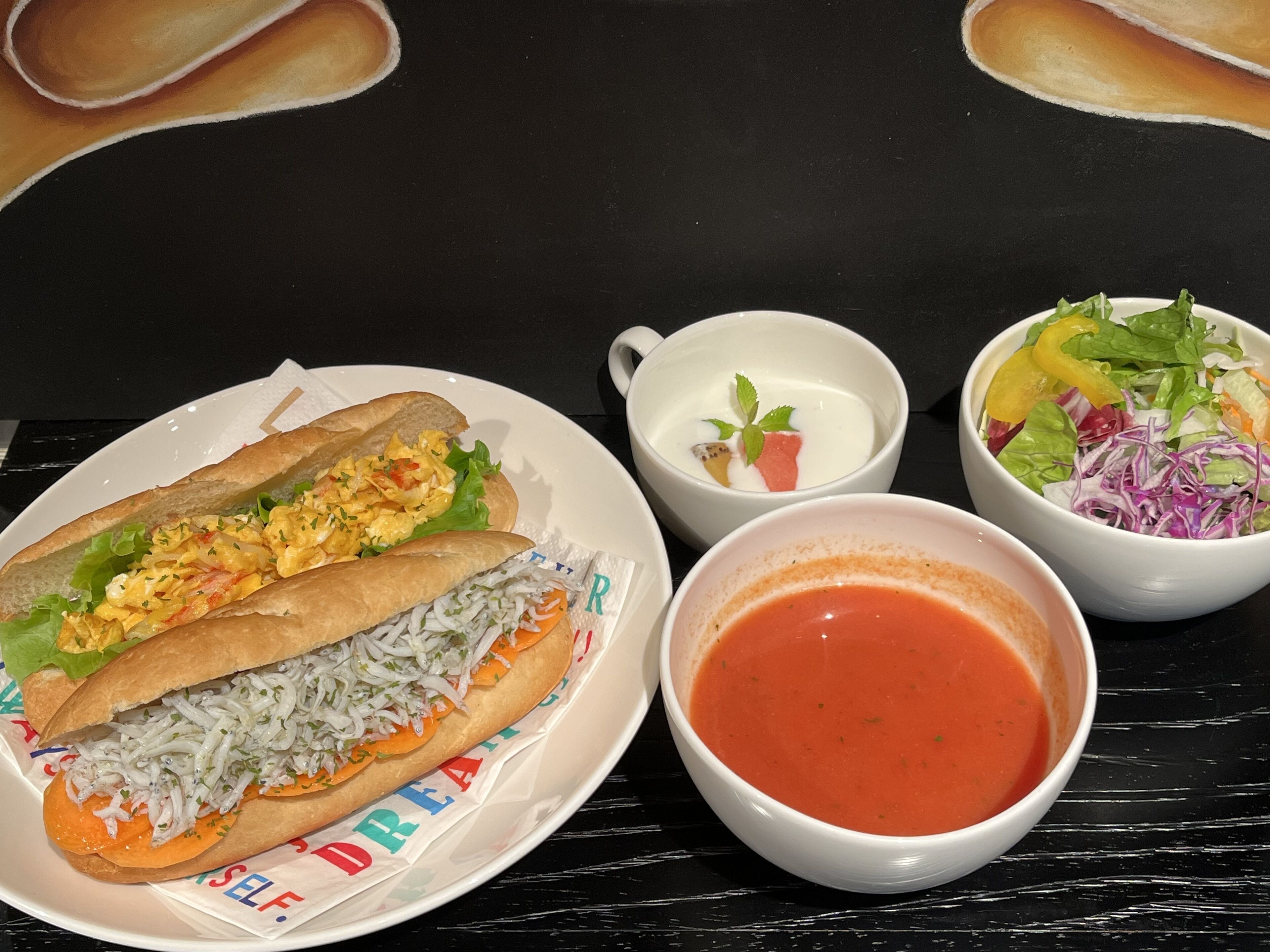 A plate with two sandwiches, a cup of soup, and a salad on a black table.