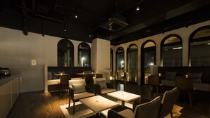 A modern lounge area with seating and tables, large arched windows, and a visible cityscape view. - Fujisawa Hotel En (Fujisawa)