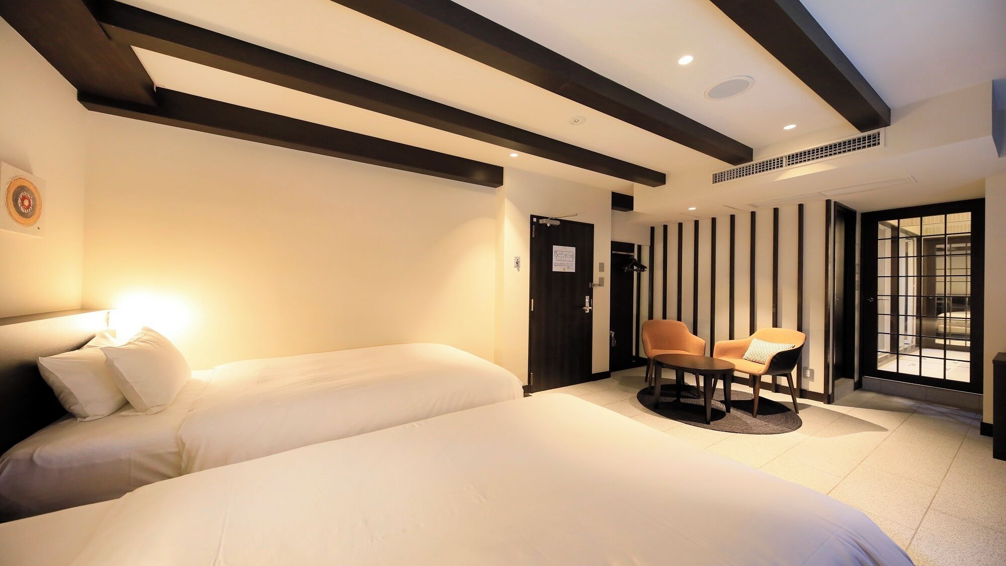 A hotel room with a large bed, a seating area with two chairs, and a view through a glass door.