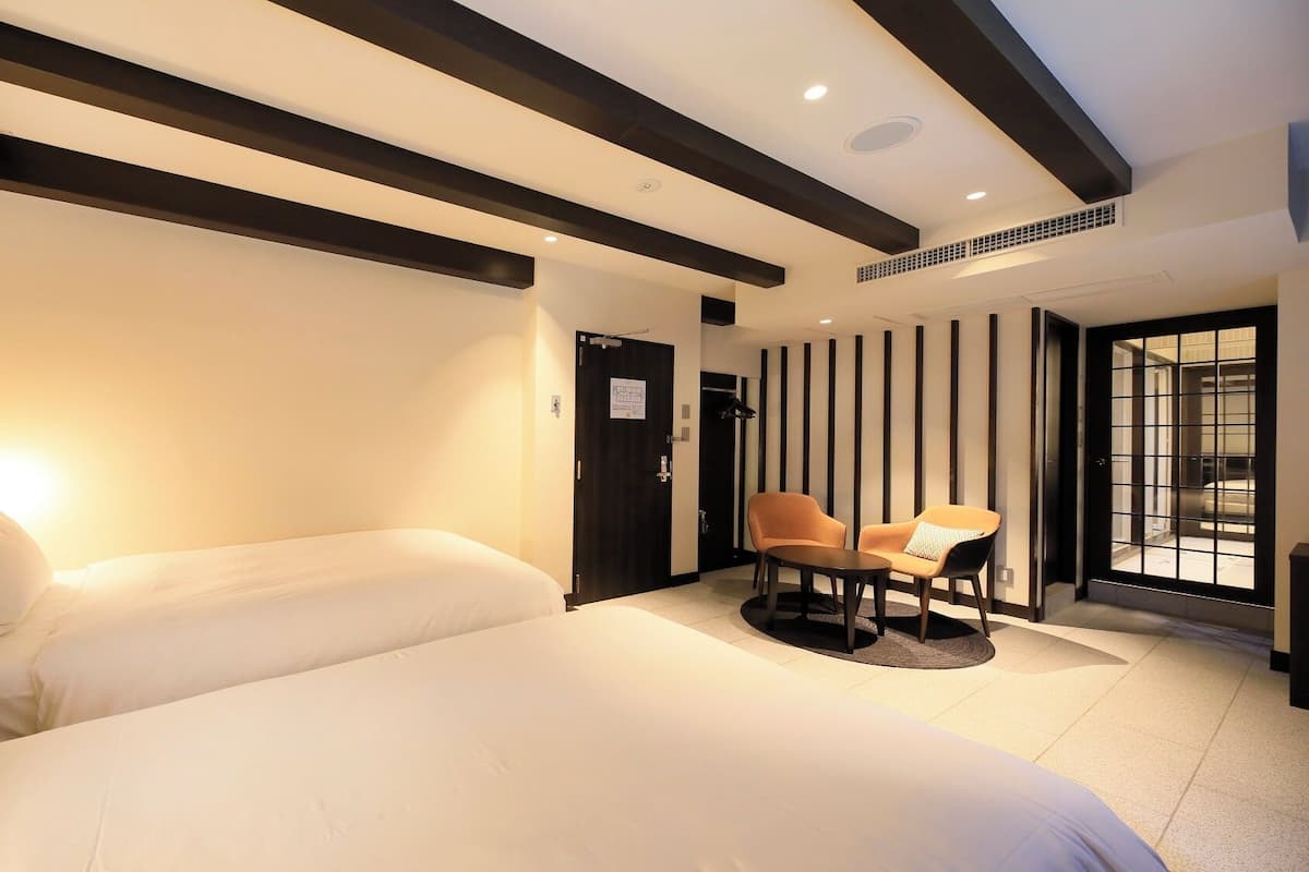 A hotel room with a large bed, a seating area with two chairs, and a view through a glass door.