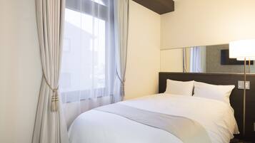 A hotel room with a large bed, a bedside table, a lamp, and a window with curtains.