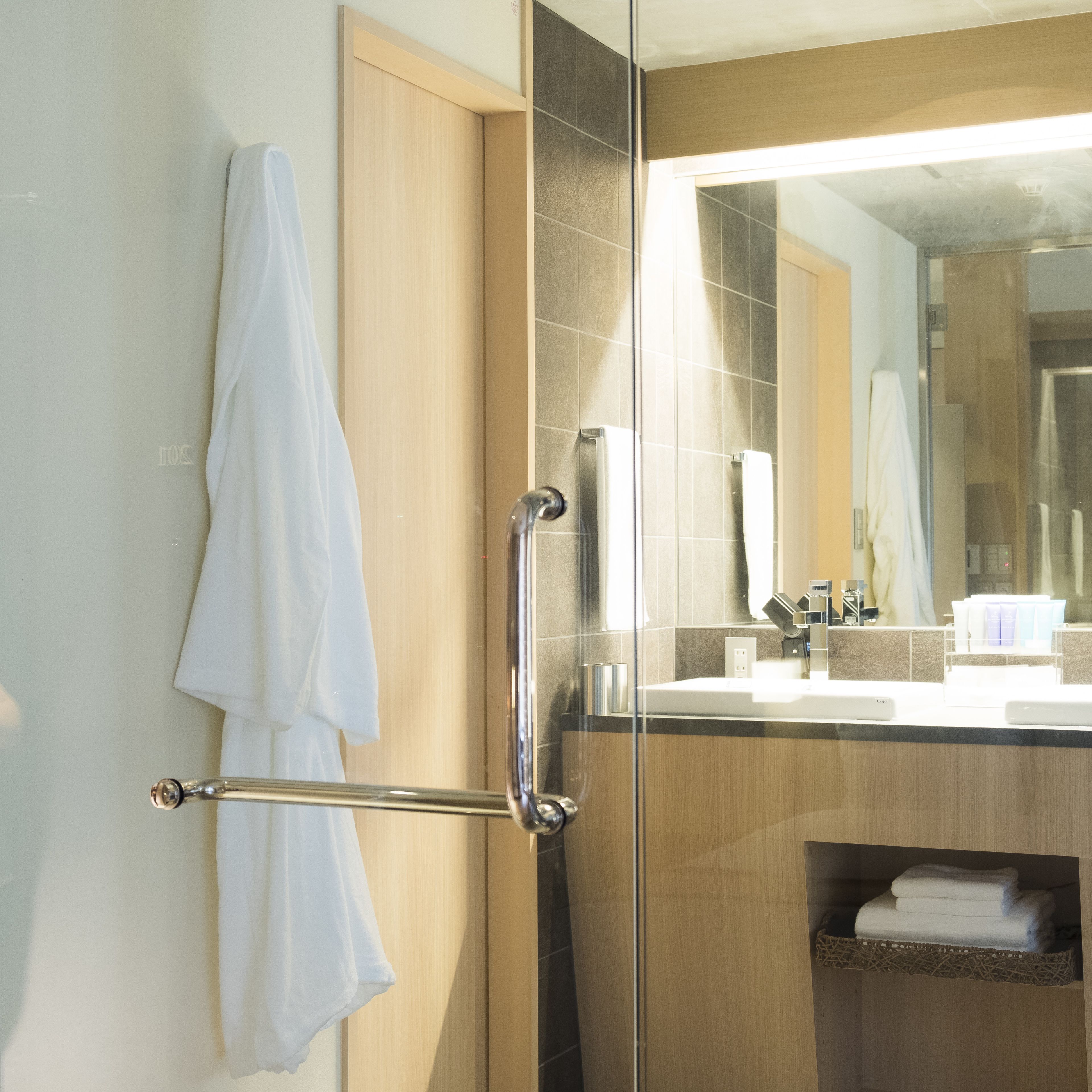 A modern bathroom with a glass shower enclosure, a wooden vanity, and a large mirror.