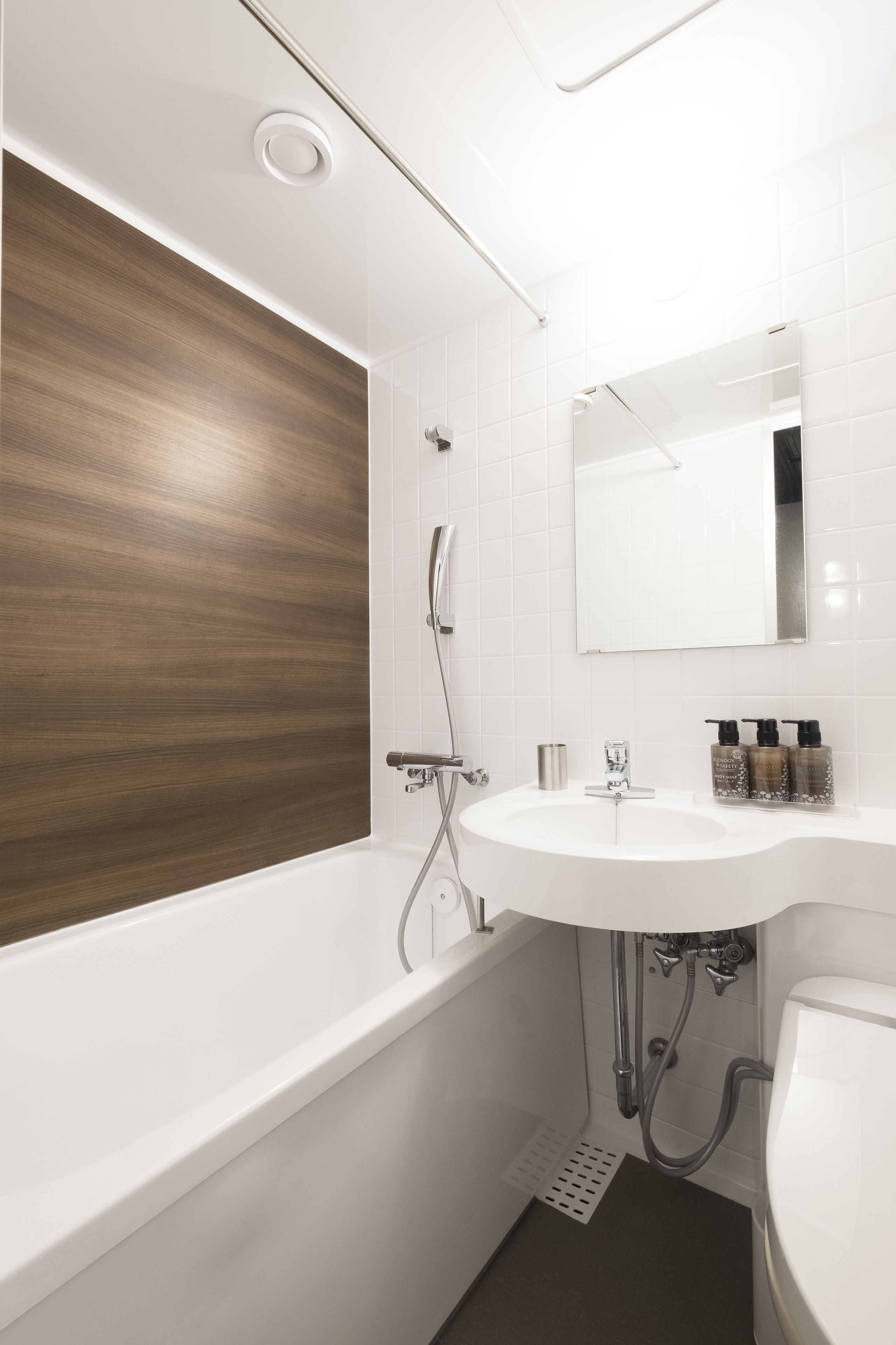 Un baño moderno con pared de paneles de madera, un lavamanos blanco, un espejo y un inodoro.