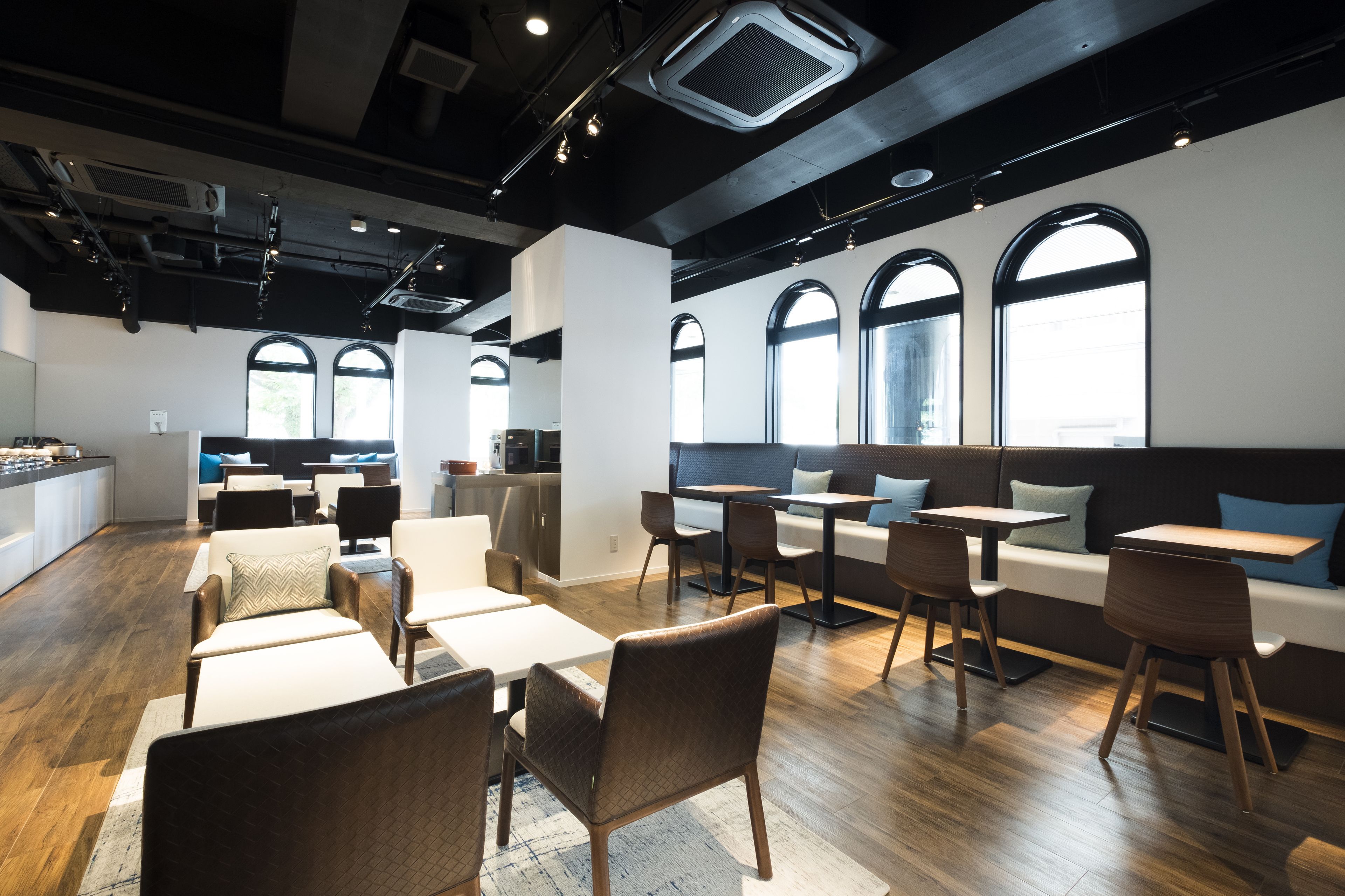 A modern cafe with wooden flooring, white and brown seating, and large arched windows.