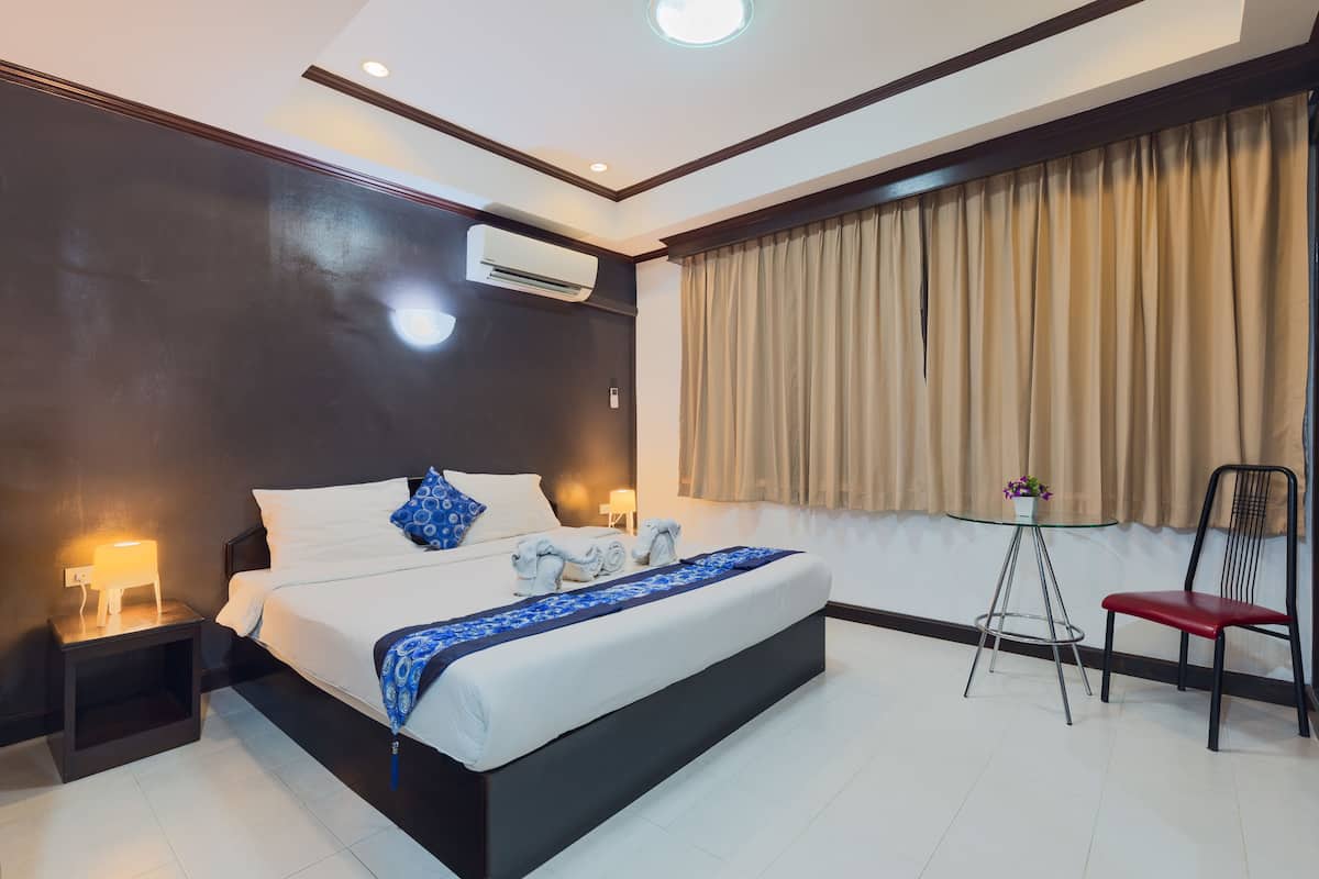 A modern hotel room with a large bed, bedside lamps, a small table with a vase, and a chair.