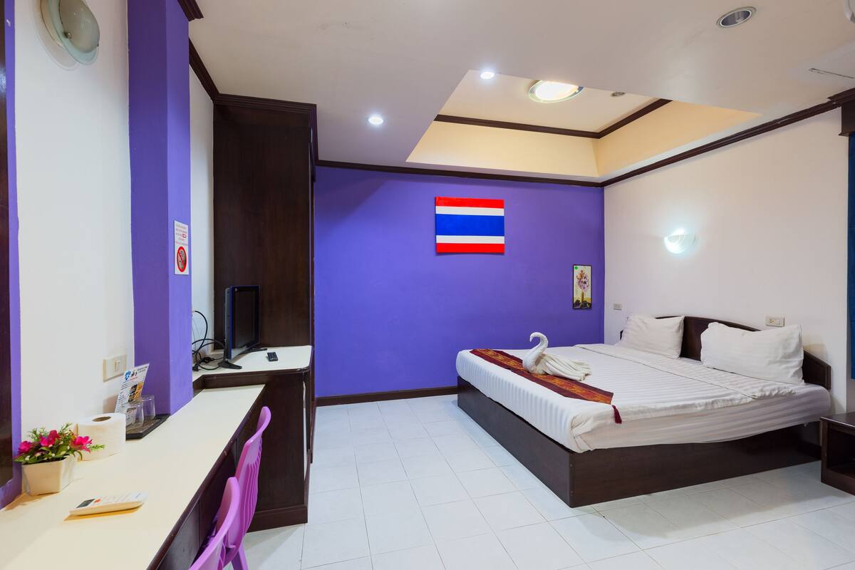 A bedroom with a bed, a desk, a chair, a flag on the wall, and a ceiling light.