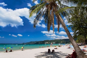 A beach with palm trees, clear blue sky, and people relaxing on the sand. - Hotel Grand Orchid Inn (Patong)