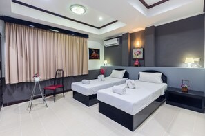 A hotel room with two beds, a small table, a chair, and a nightstand with a lamp. - Hotel Grand Orchid Inn (Patong)