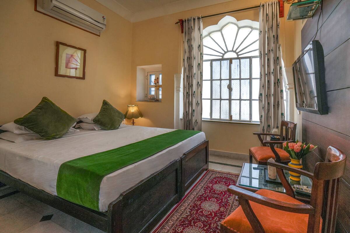Une chambre d’hôtel équipée d’un lit, d’un bureau, d’une chaise, d’une télévision, d’une fenêtre avec des rideaux et d’un climatiseur.