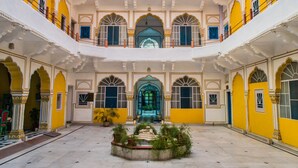 A spacious courtyard with a central fountain, surrounded by yellow and white walls with arched doorways and windows.