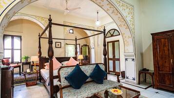A four-poster bed with a canopy, a sofa with floral upholstery, a wooden coffee table, and a traditional wooden wardrobe.