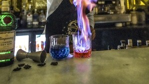 A bartender pouring a flaming drink into a glass.