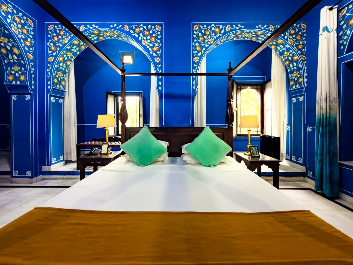A room with a large bed, two nightstands, a window with curtains, and blue floral wall decorations.