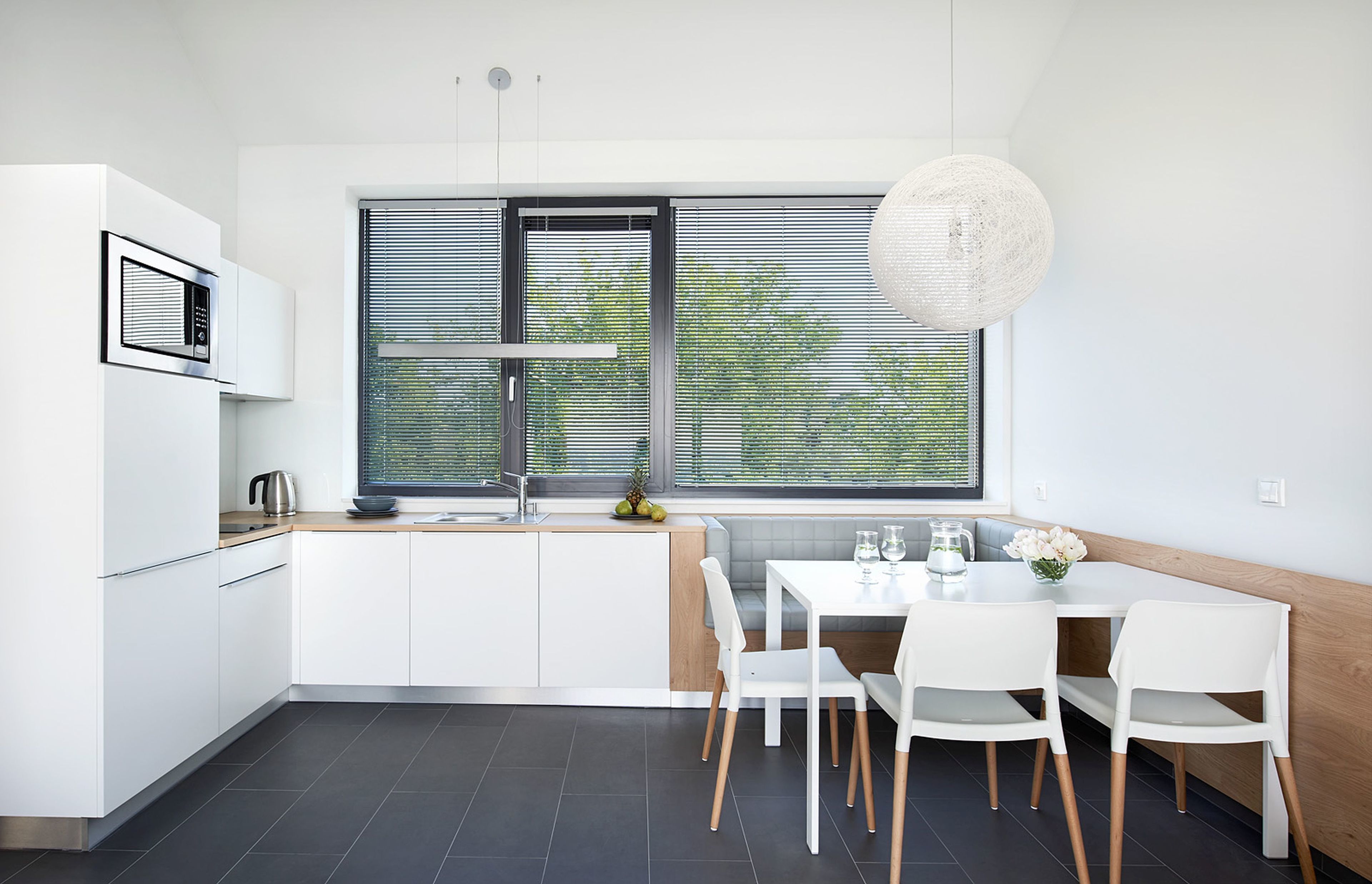 A modern kitchen with white cabinetry, a built-in oven, and a large window with blinds.