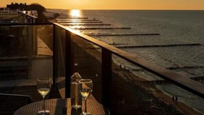 Mesa con dos vasos y una botella, con vista a una playa al atardecer.