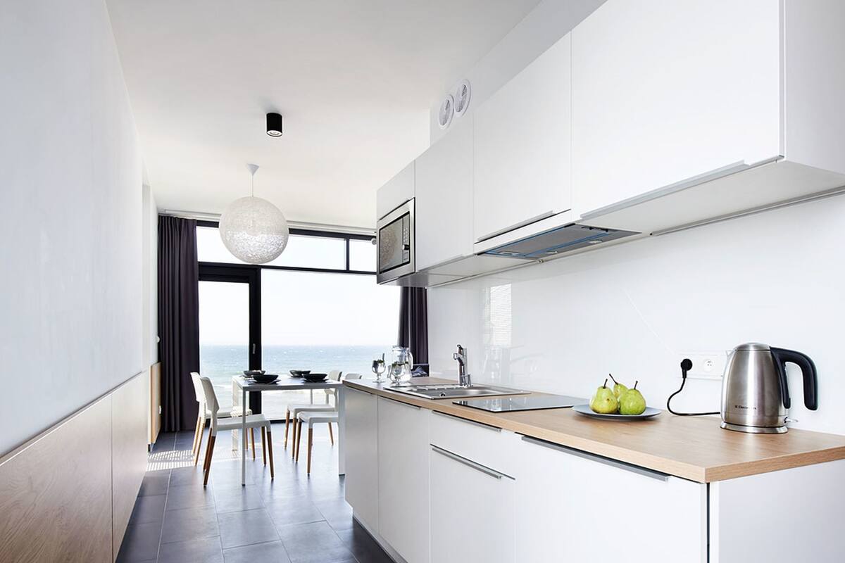 A modern kitchen with white cabinets, a wooden countertop, and a view to the outside.