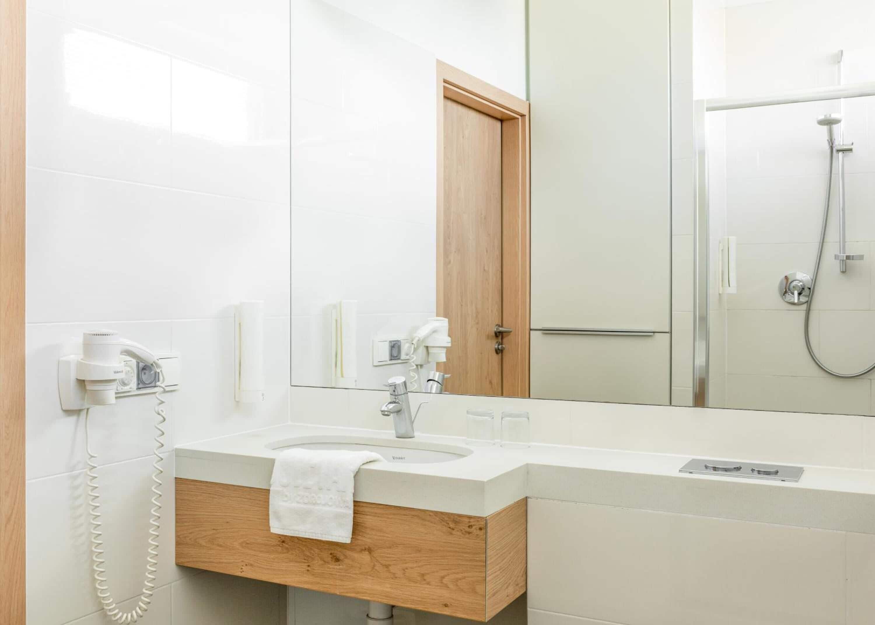 A modern bathroom with a wooden vanity, a mirror, a sink, and a shower area.