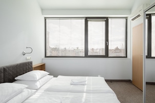Una habitación de hotel con una cama, dos ventanas, una mesita de noche y un armario.