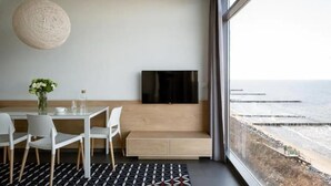Una habitación moderna con un ventanal grande, un televisor de pantalla plana, una mesa de comedor con sillas y un banco.