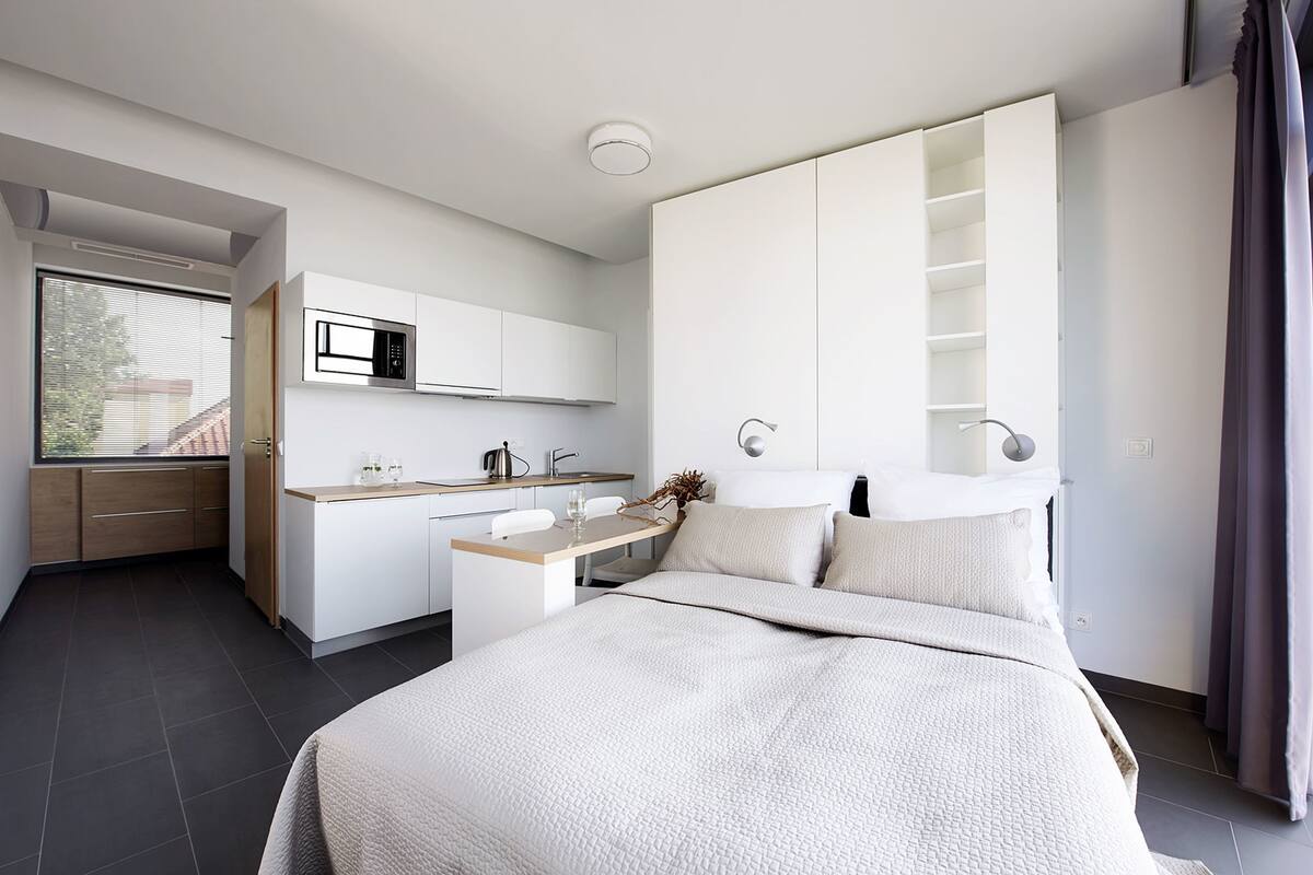 A modern bedroom with a large bed, a built-in desk, a microwave, and a wardrobe.