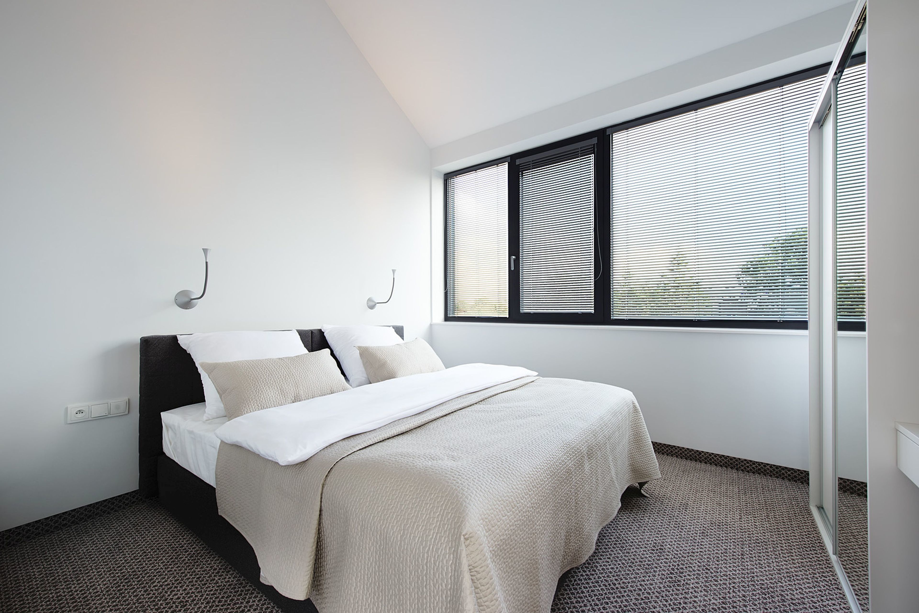 Ein modernes Schlafzimmer mit einem Bett, einem Fenster mit Jalousien und einer Steckdose an der Wand.