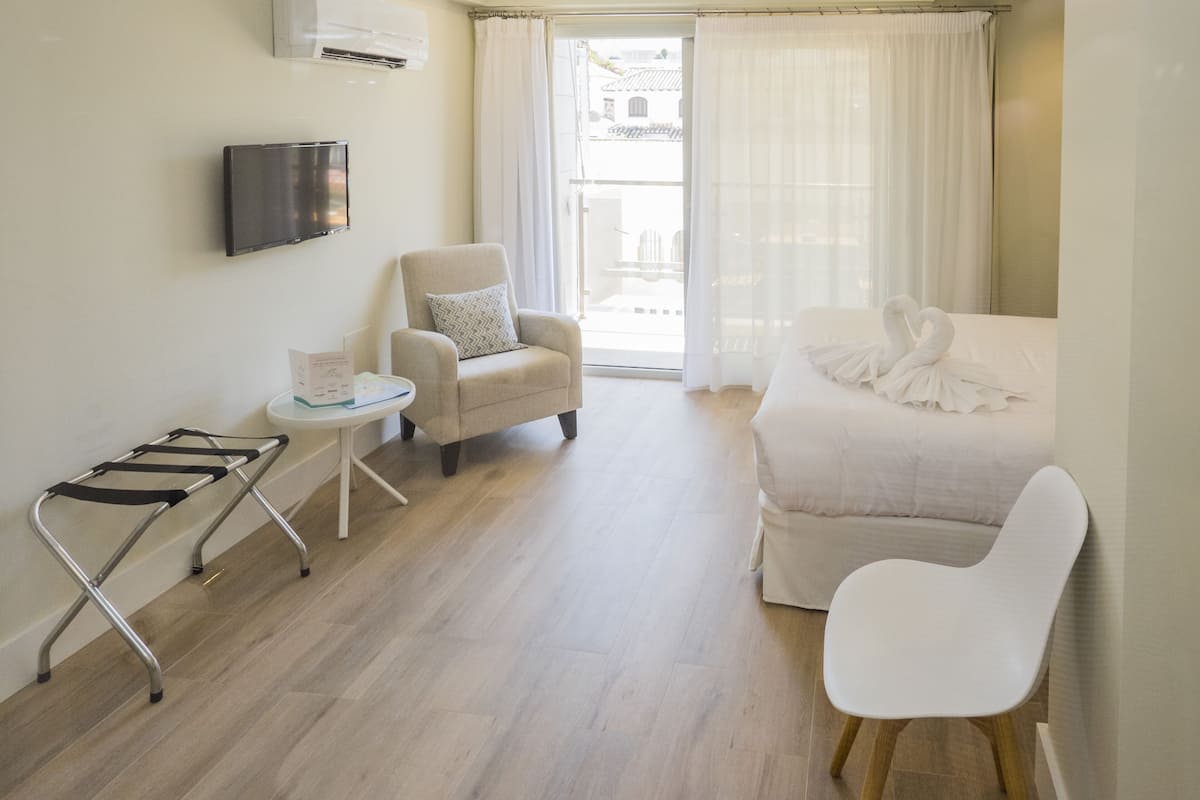 A hotel room with a bed, a chair, a small table, and a TV mounted on the wall.
