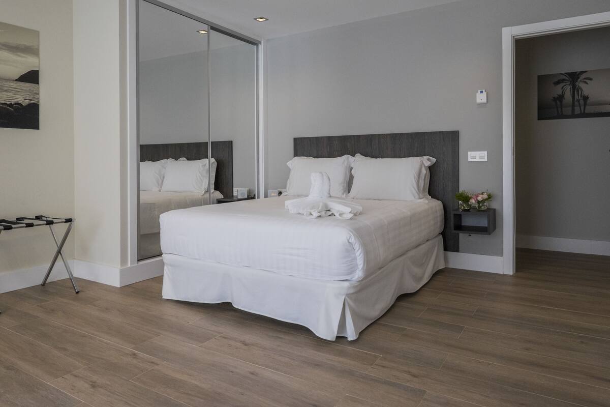 A modern hotel room with a large bed, a glass door leading to a balcony, and a small bedside table with a lamp.