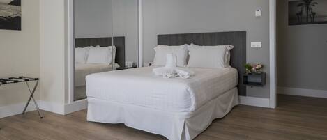A modern hotel room with a large bed, a glass door leading to a balcony, and a small bedside table with a lamp.