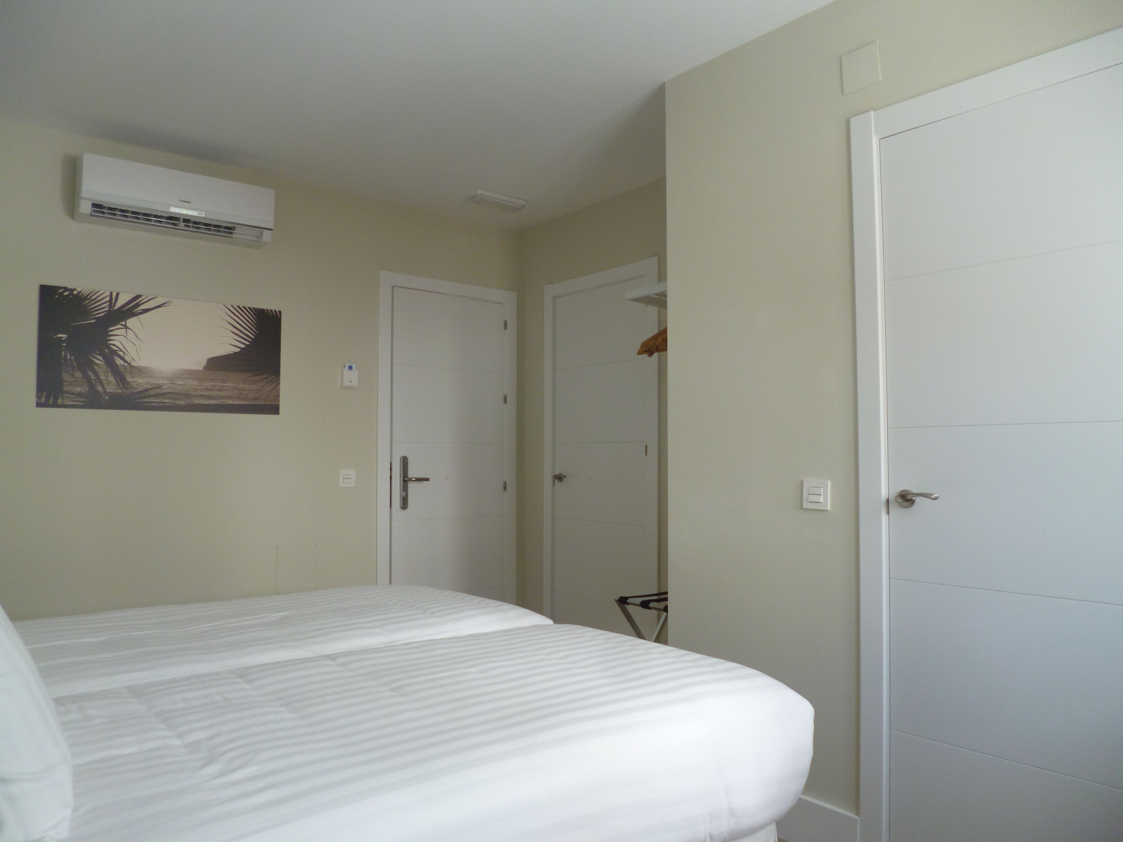 A bedroom with a bed, an air conditioning unit, a door, and a wall-mounted picture.