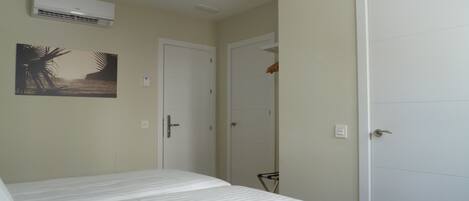 A bedroom with a bed, an air conditioning unit, a door, and a wall-mounted picture.