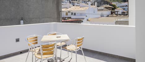 Un balcon avec une table et des chaises, donnant sur un quartier résidentiel avec des bâtiments blancs et une colline.