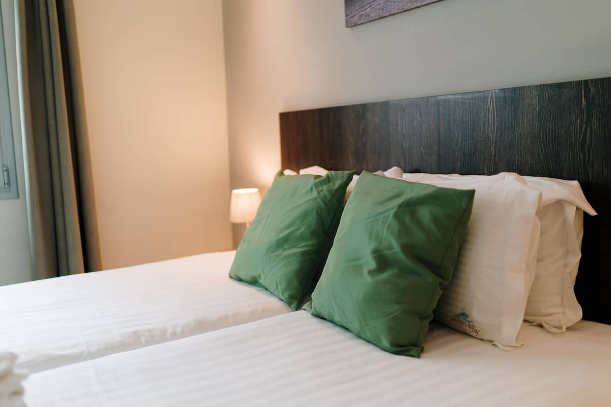 A hotel room with two beds, each with white bedding and green and white pillows.