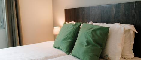 A hotel room with two beds, each with white bedding and green and white pillows.