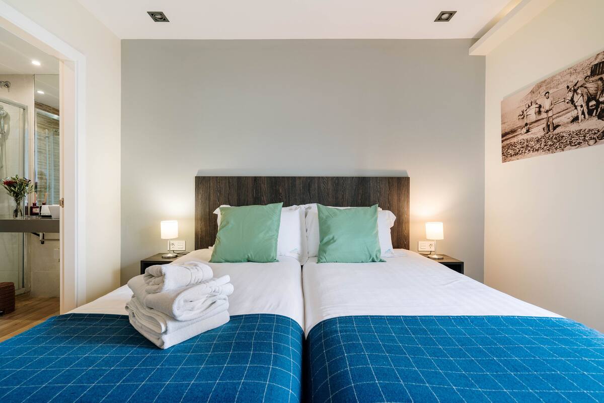 A double bed with green and white bedding, two bedside tables with lamps, and a wall-mounted picture.