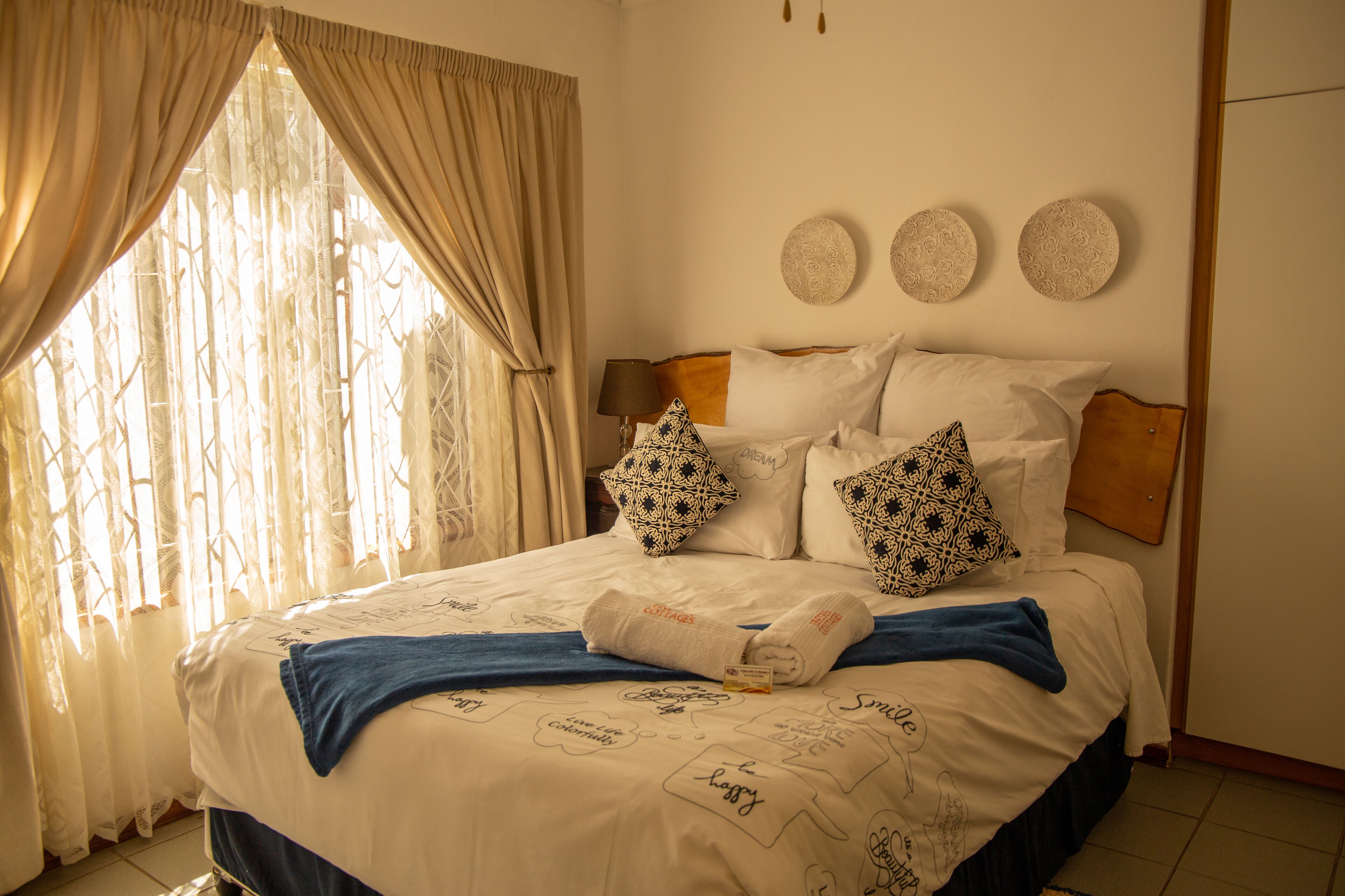 A neatly made bed with a blue blanket, a pair of towels, and decorative pillows. There are three wall-mounted decorative plates above the bed.
