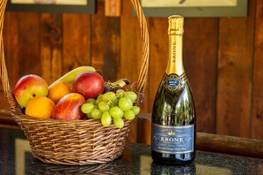 A bottle of Krone 2019 Brut wine next to a wicker basket filled with fruits.