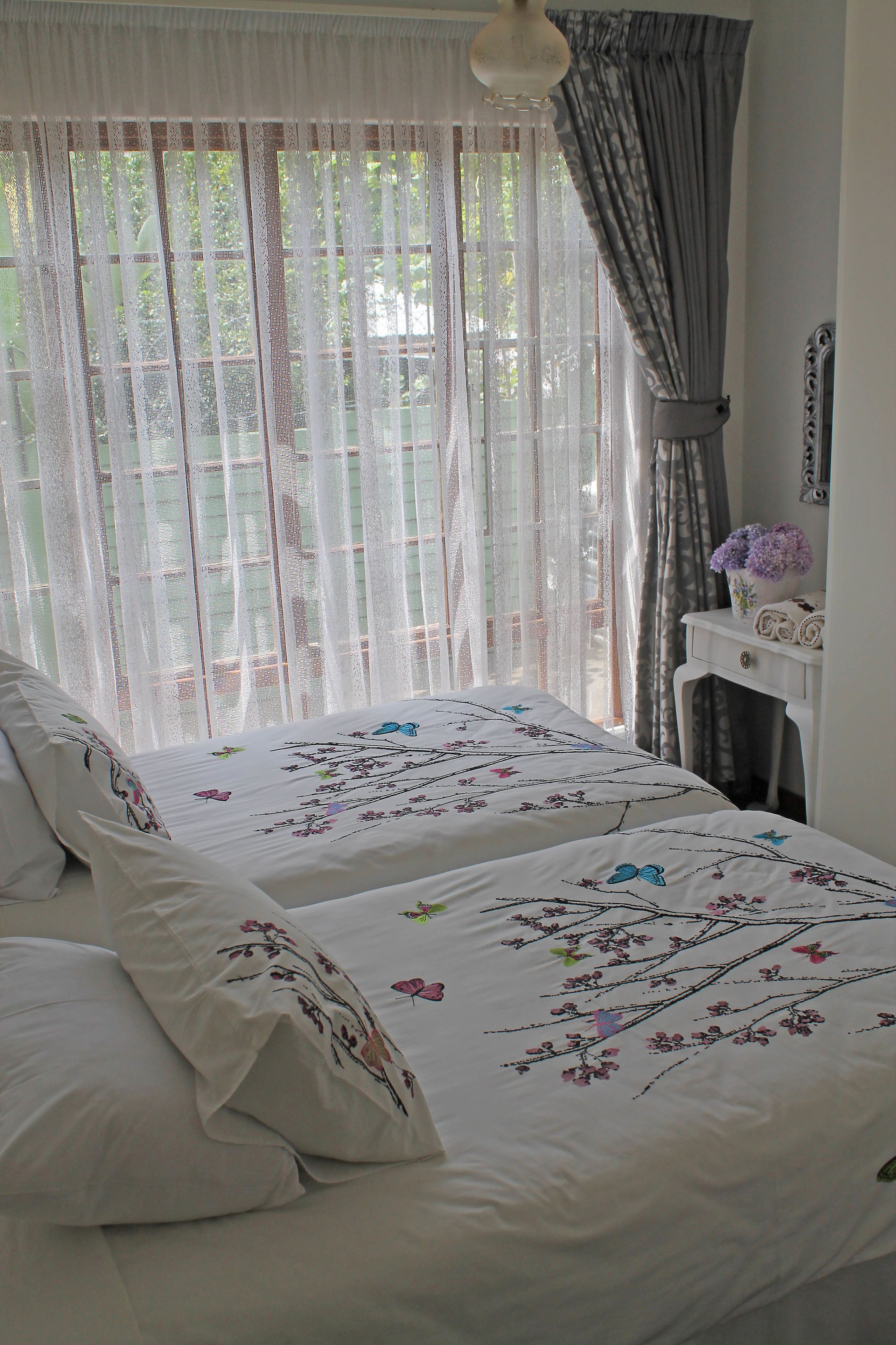 A bedroom with two beds, a dresser, and a window with sheer curtains.
