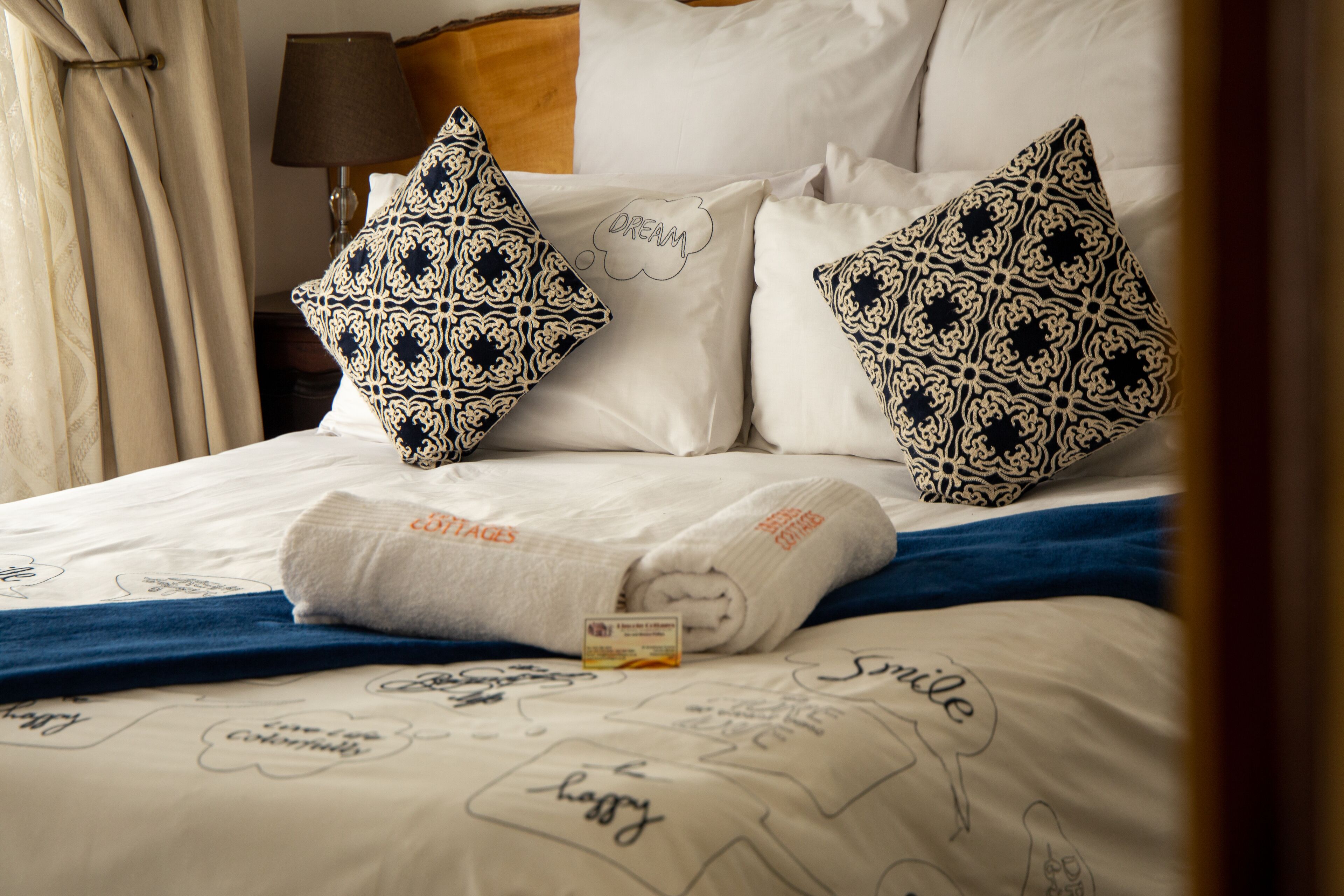 A neatly made bed with patterned pillows, a folded towel, and a card on the bed.