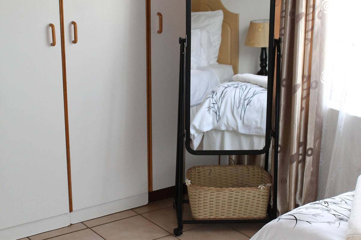 A bedroom with a bed, a wardrobe, a mirror, and a wicker basket.