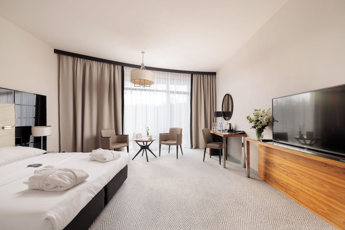 A hotel room with a bed, a desk, a TV, and a large window with curtains.
