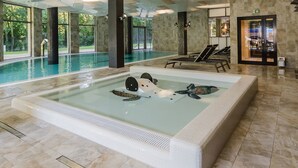 A modern indoor pool area with a hot tub, lounge chairs, and a stone wall. - Diune Hotel (Kolobrzeg)