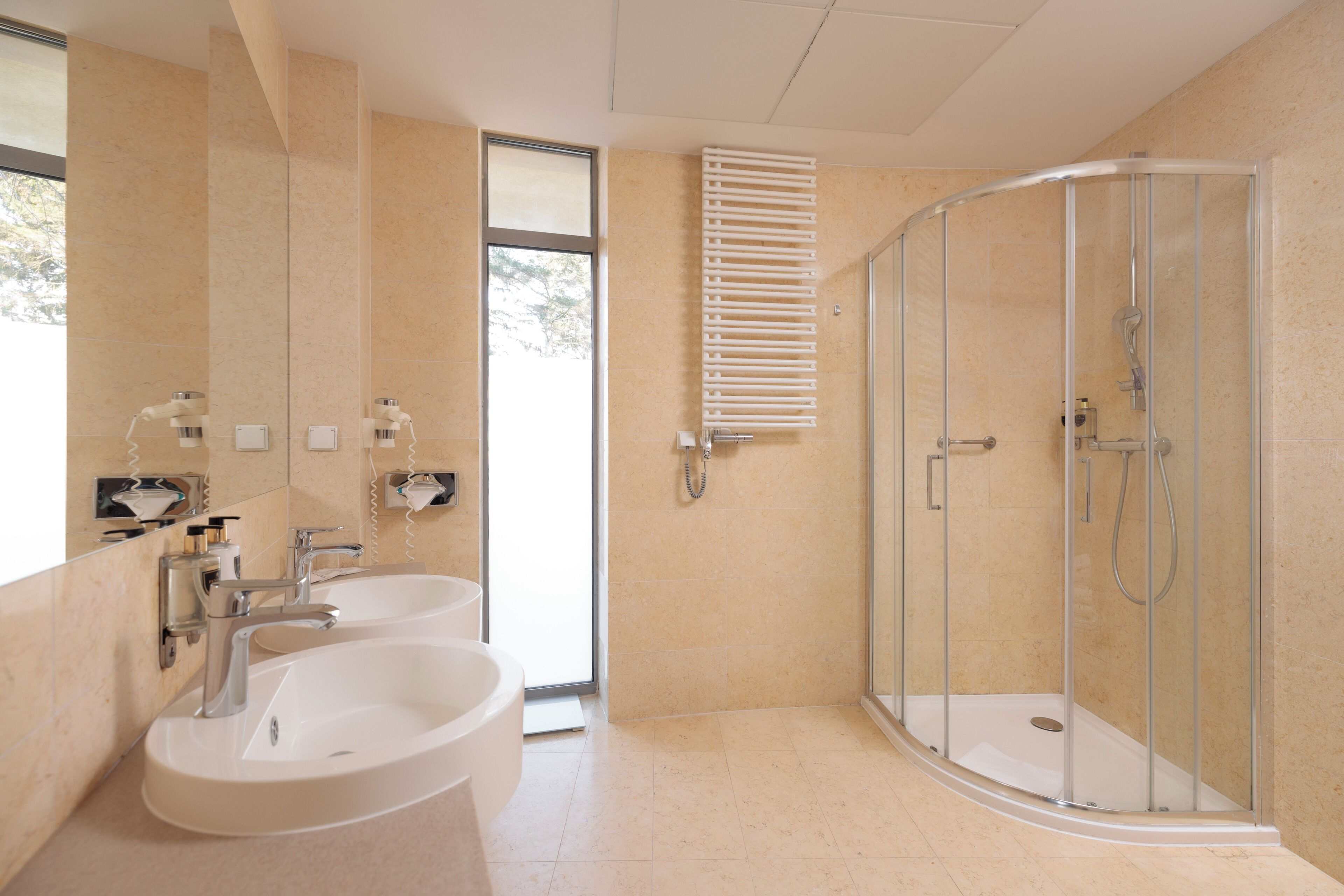 A modern bathroom with two sinks, a glass shower enclosure, and a large window.