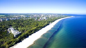 An aerial view of a coastal area with a long sandy beach, dense greenery, and a mix of residential and commercial buildings. - Diune Hotel (Kolobrzeg)