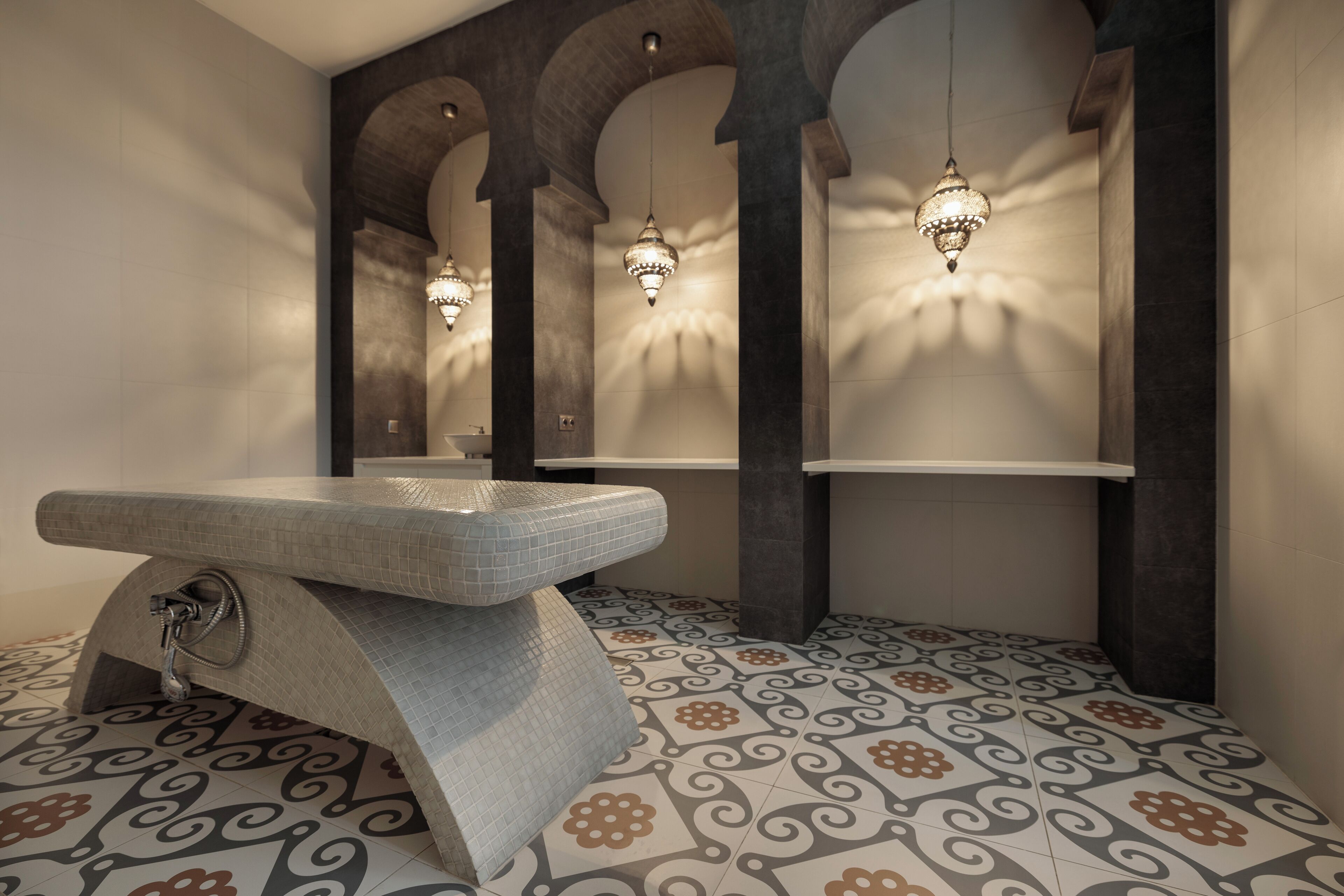 Een moderne badkamer met een unieke tegelvloer, een grote spiegel en decoratieve verlichting.