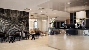 A modern lobby with a marble wall, seating area, reception desk, and a chandelier. - Diune Hotel (Kolobrzeg)